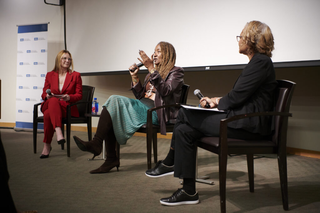 Holly Mitchell on stage with moderators speaking to an audience