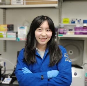 Zenya Bian, Goldwater Scholarship winner, poses in a laboratory wearing a blue lab coat and gloves